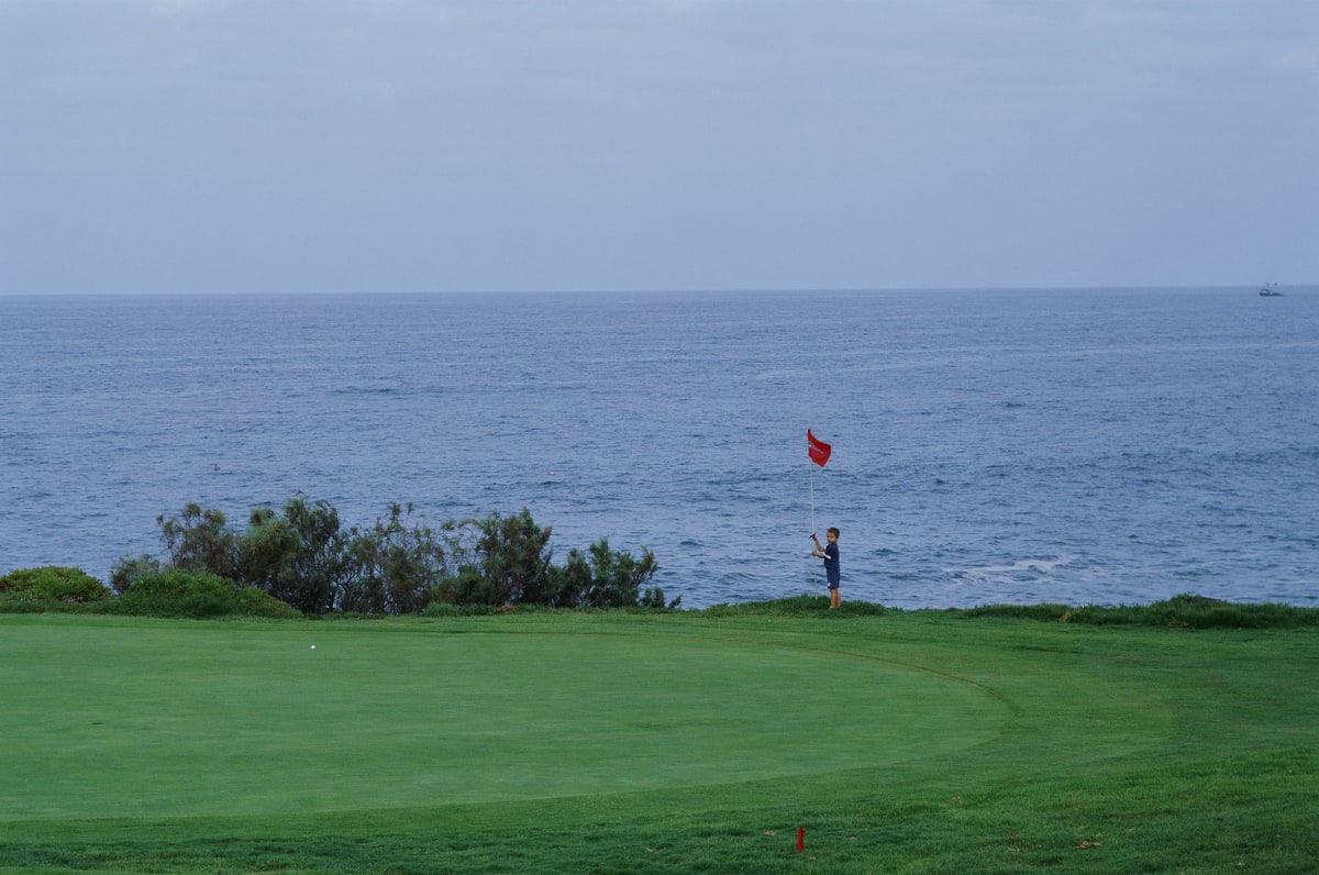 Baker stands beside a red flag on a green overlooking the ocean.