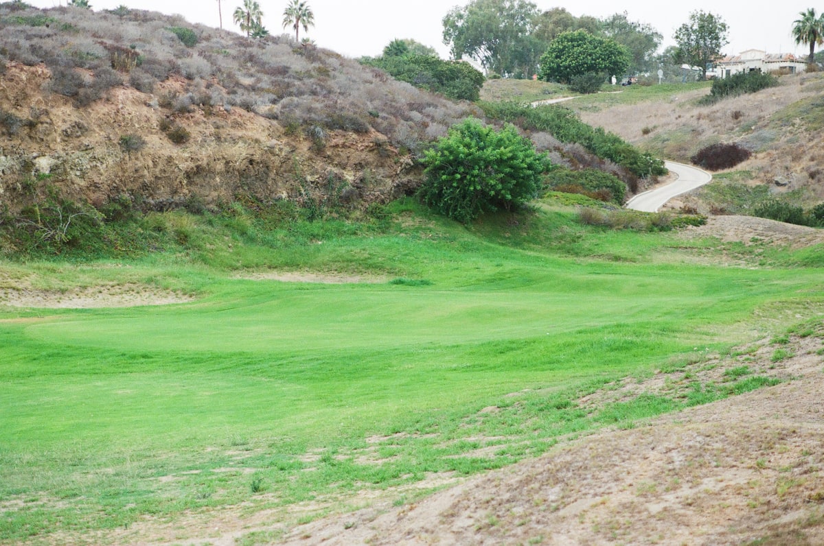 The maintained former eighteenth green sits in a rocky hollow beneath a winding cart path.