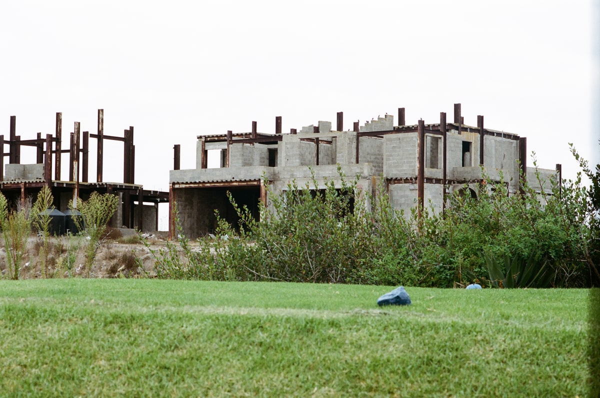 Vacant unfinished concrete-block buildings and exposed steel border the golf course.