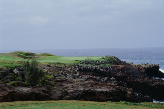 A red flag and green beyond rugged coastal rocks, with the ocean behind.