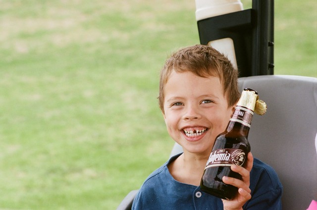 Baker smiles in the golf cart while holding a brown bottle with a torn gold wrapper.