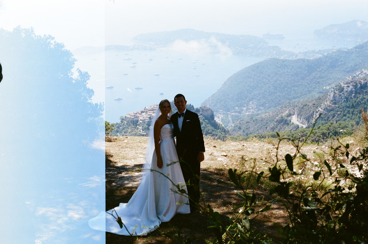 A couple in wedding clothes above the coast, with a light leak along the left edge