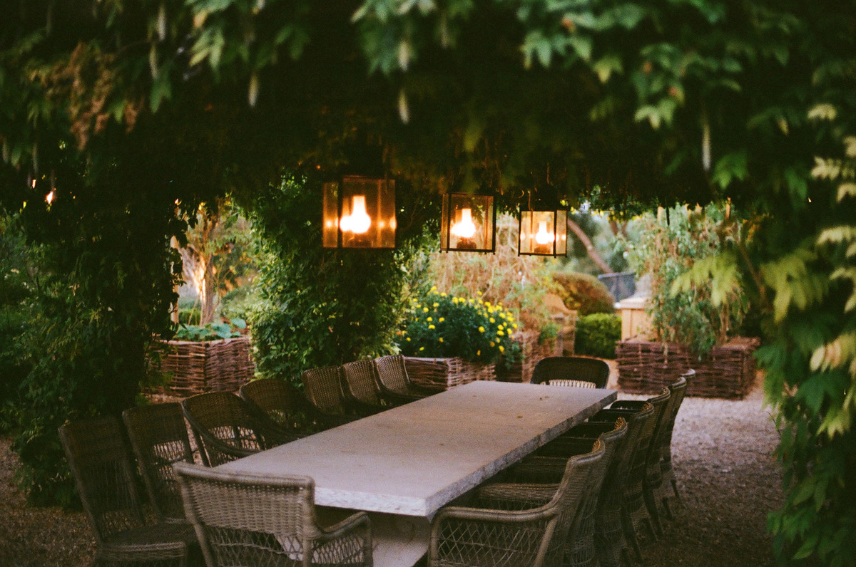 A long outdoor table beneath green foliage and hanging lanterns