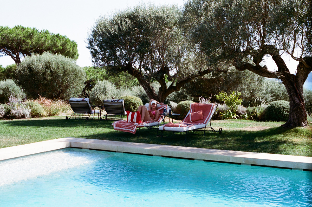 A person resting on a lounge chair beneath trees beside a pool