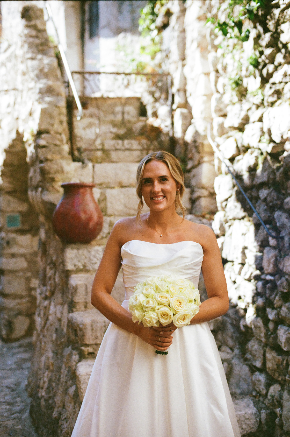 A bride holding a bouquet in a narrow stone passage
