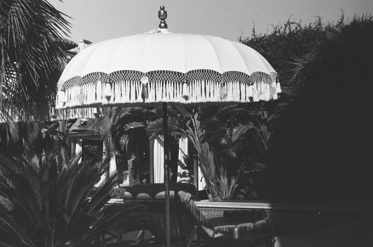 A fringed umbrella above garden seating, photographed in black and white