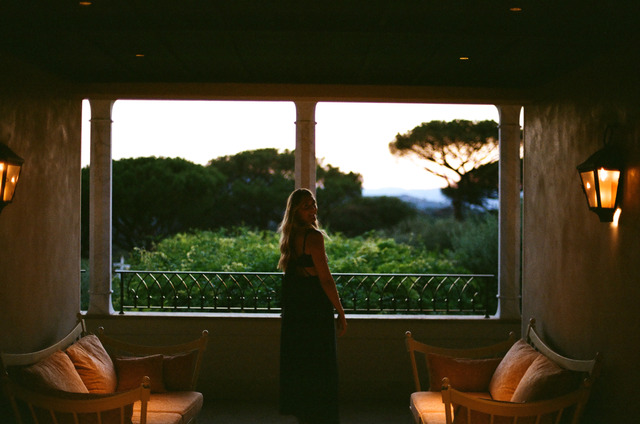 A woman in a dark dress standing on a covered terrace at dusk