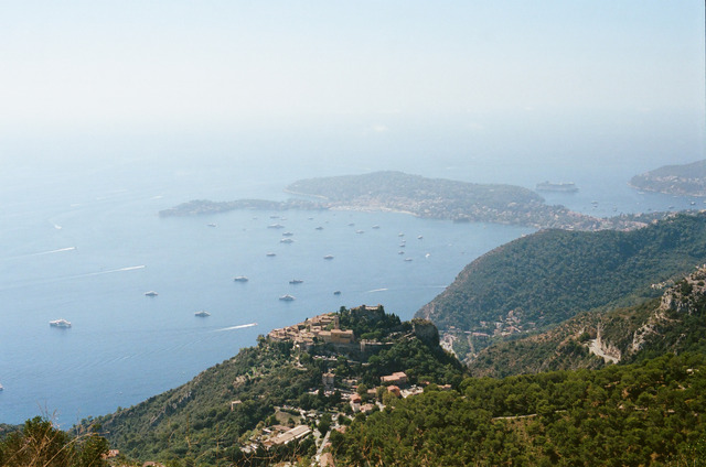 A broad view of the coast, a hilltop village, and boats on the water