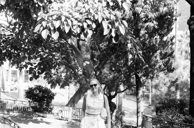 A woman in sunglasses beneath a tree, photographed in black and white