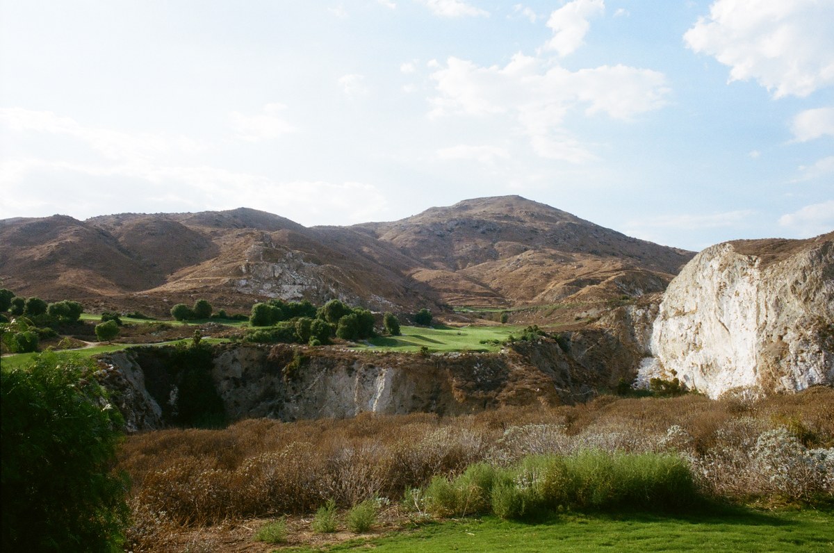 Fairways and brown hills beyond a deep quarry, with a bright white rock face at right