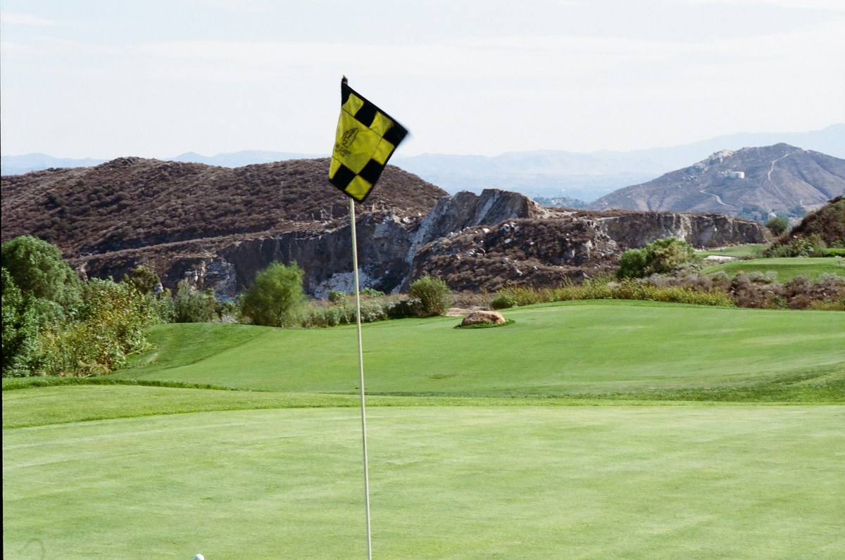 A yellow and black flag in the foreground, with a boulder beside the green and distant quarry faces and hills